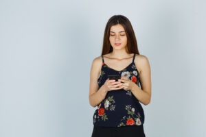 young woman looking at smartphone in blouse and looking busy , front view.